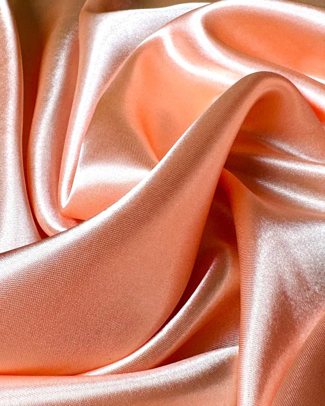 Close-up of smooth, pink peach scarf fabric with folds