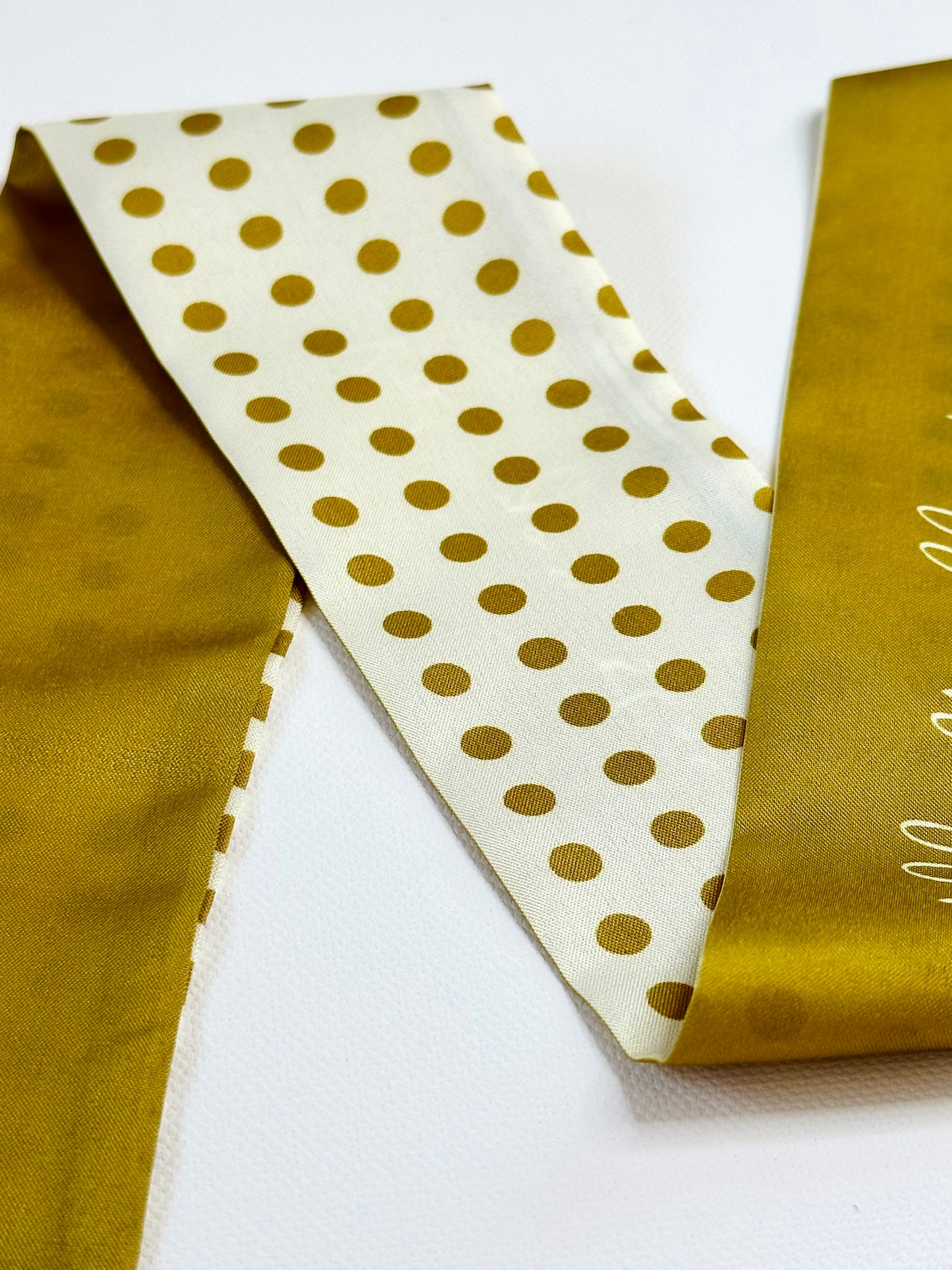 Gold polka dot ribbon scarf on a white background