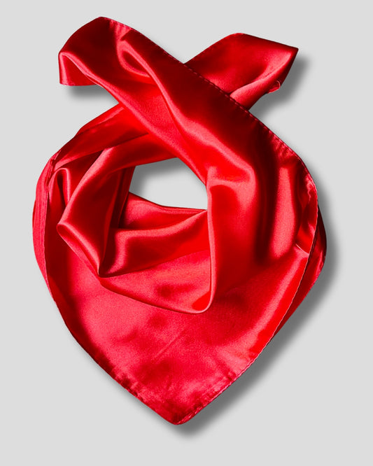 Red satin scarf folded into a heart shape on a light gray background