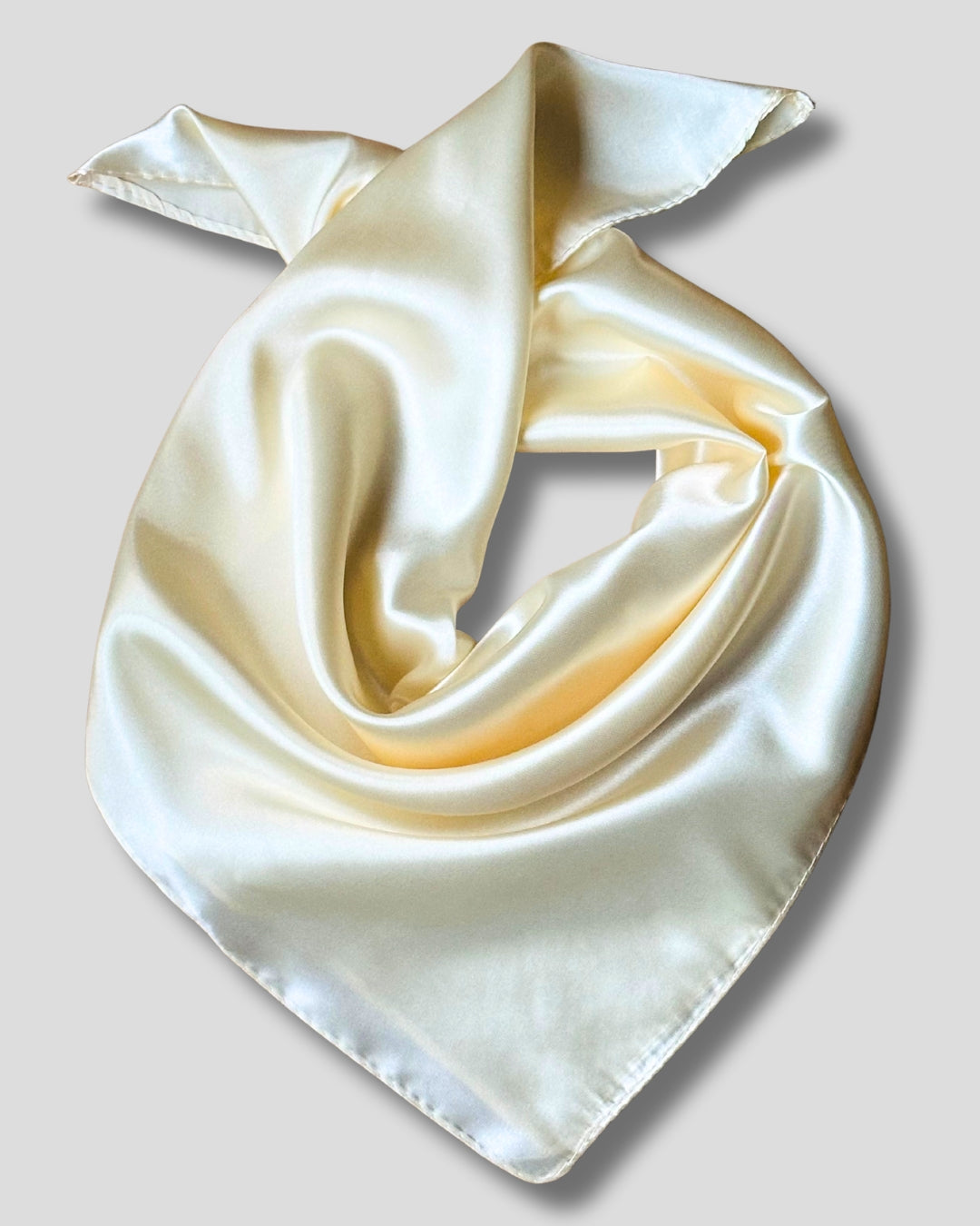 Cream-colored silk scarf folded into a triangle on a light gray background